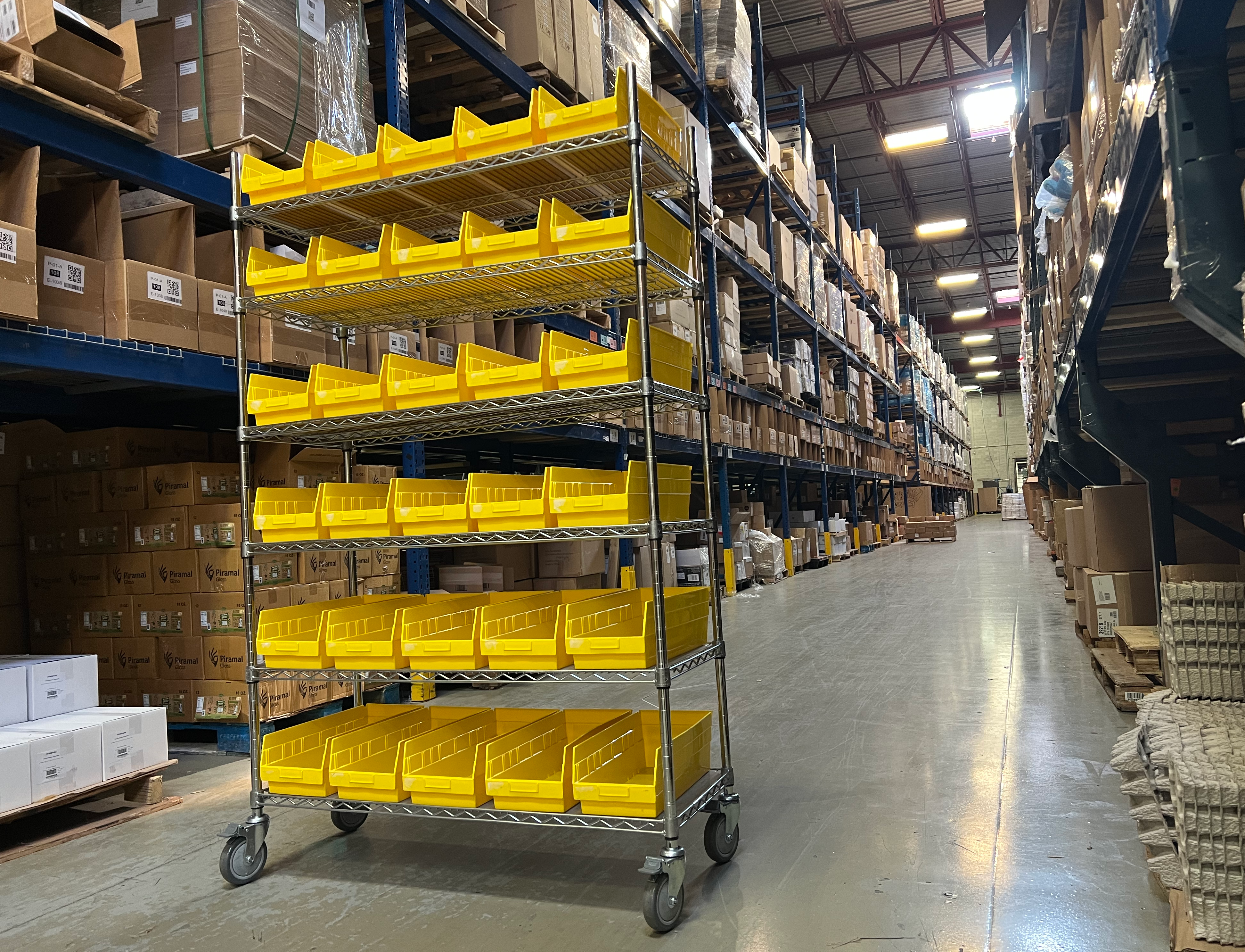 Metal cart full of small yellow bins, in the middle of a warehouse aisle